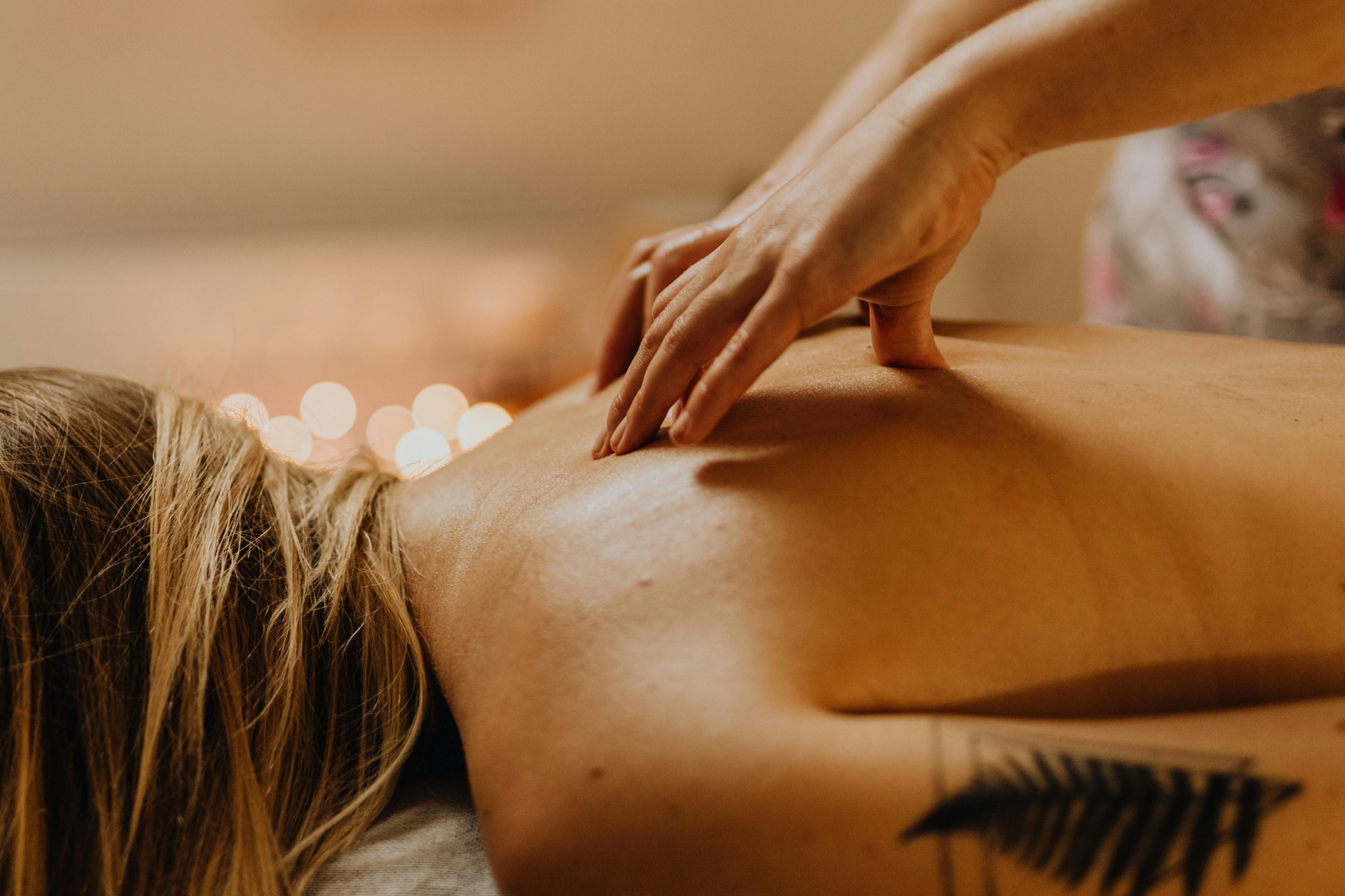 Hand gently massaging a person's bare back in a warm, spa-like setting