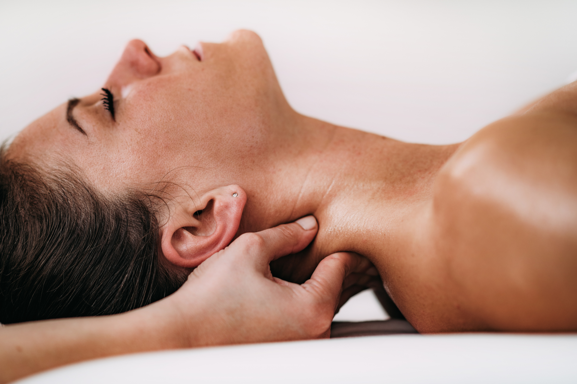 Person lying face up while a hand massages the neck on a treatment table