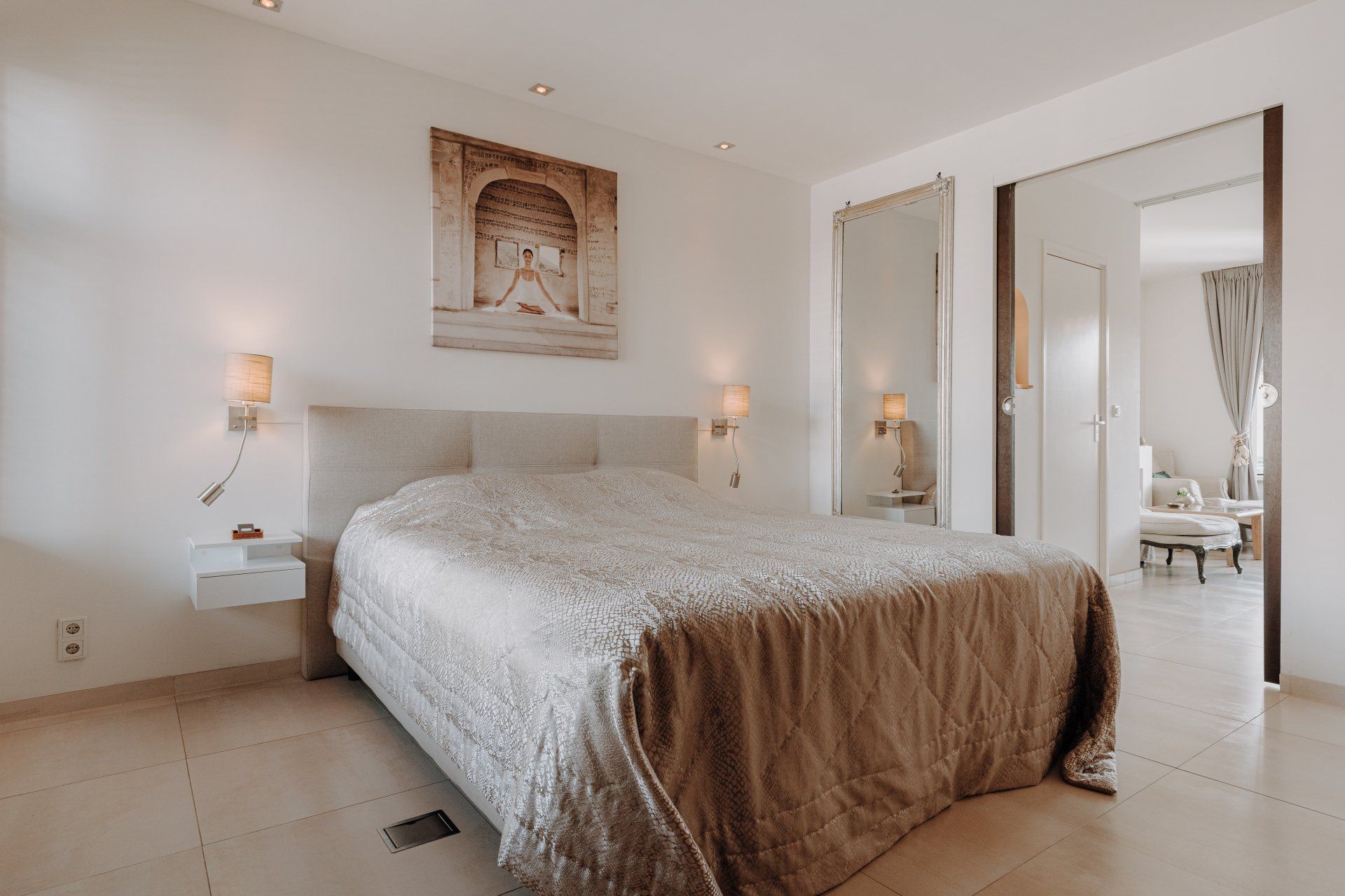 Slaapkamer met een groot bed, decoratieve kunst en een schuifdeur naar een zithoek.