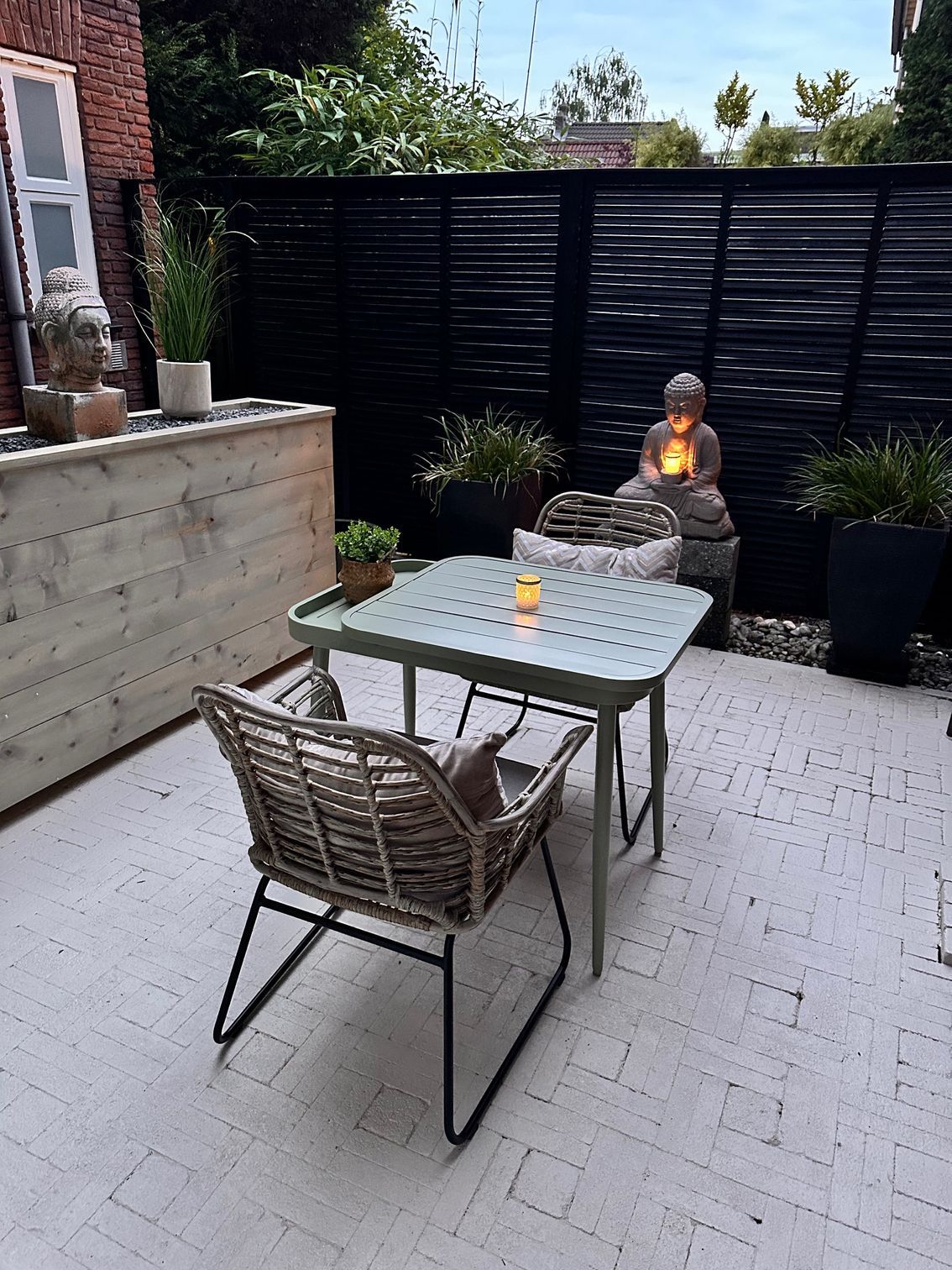 Buitenpatio met een tafel, stoelen, Boeddhabeeld en een zwarte shutters.