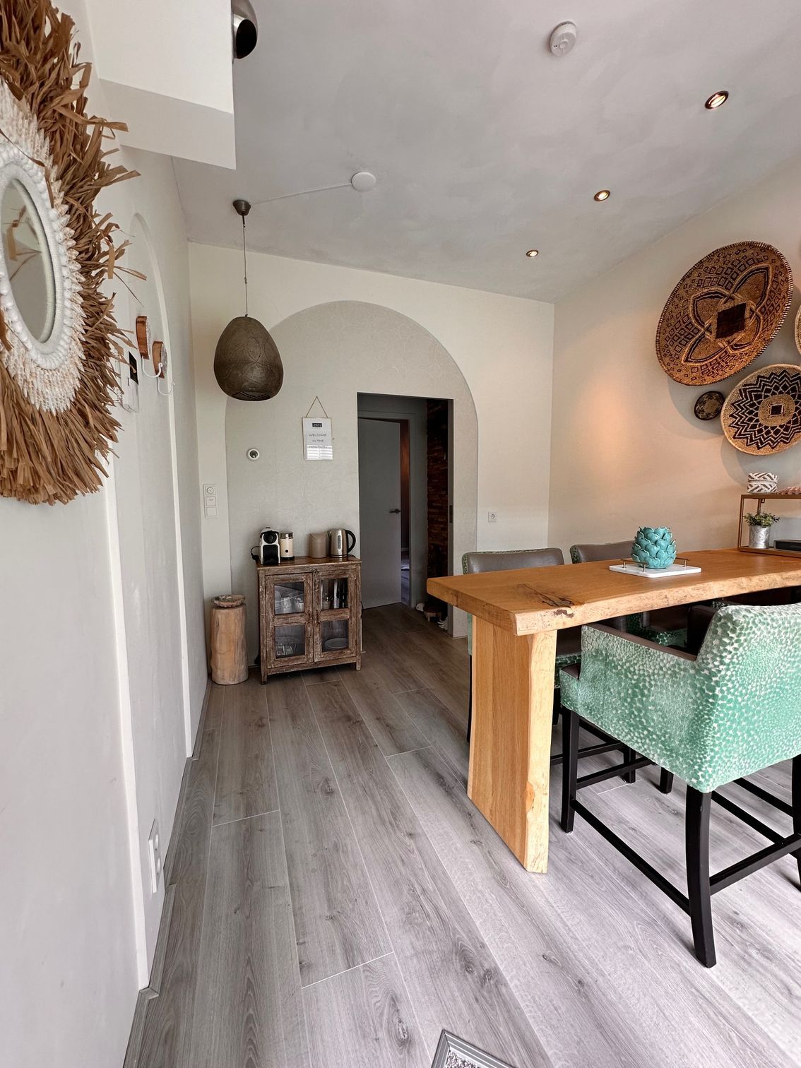 Eethoek met houten tafel, groene stoelen en decoratieve wandobjecten.