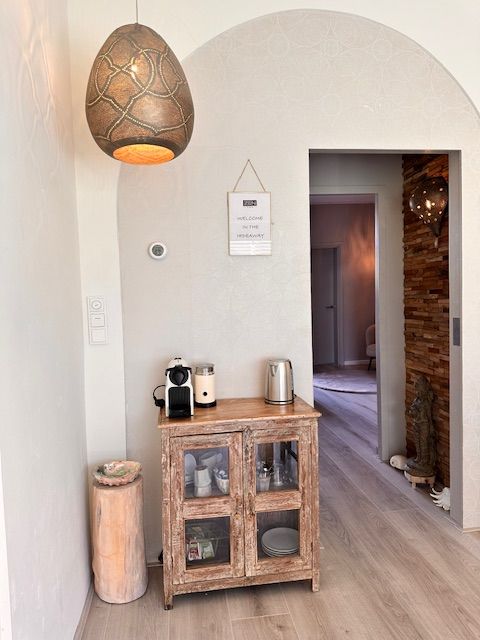 Houten kast met koffiezetapparaat, waterkoker en decoratieve lampen in een boogvormige deuropening.