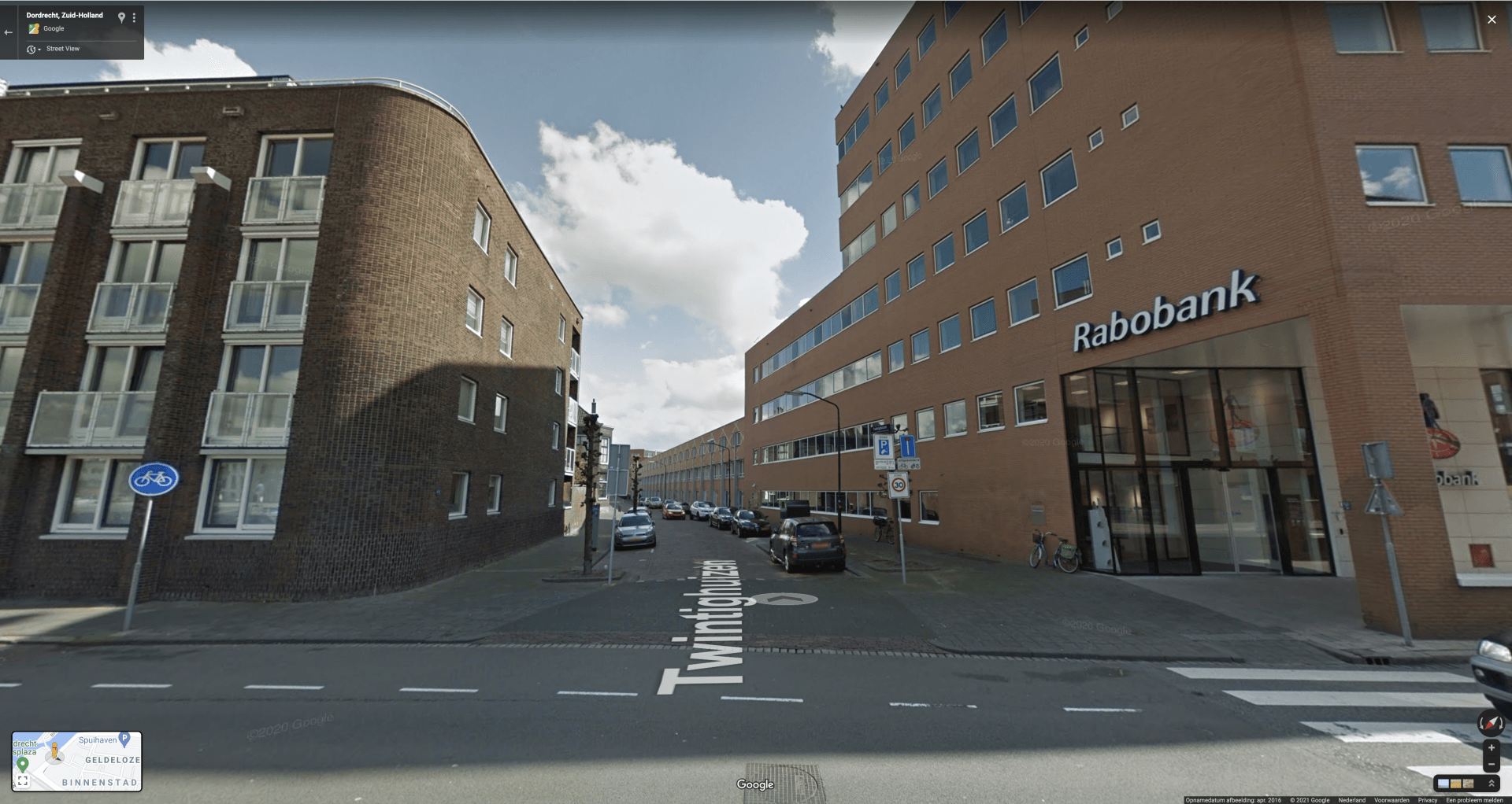 Straatbeeld met bakstenen gebouwen en een bank met het opschrift 