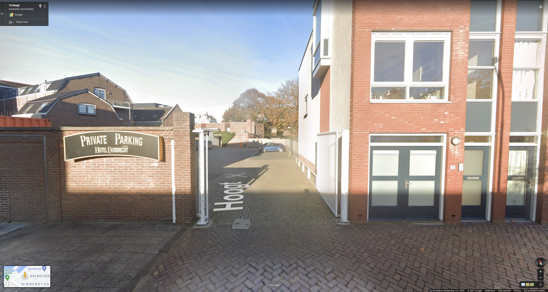 Een bakstenen gebouw en een stoep met een bord waarop 'Openbare parkeerplaats' staat. Blauwe lucht.