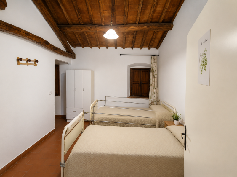 Piccola camera da letto con due letti singoli, pareti bianche, soffitto in legno e una finestra in fondo.
