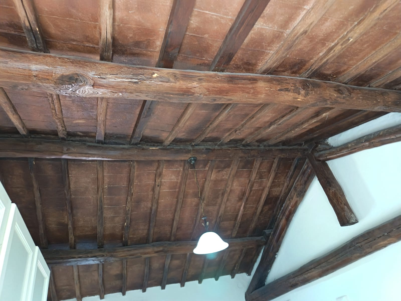 Soffitto in legno con travi a vista e lampadario bianco sospeso all'interno di una stanza