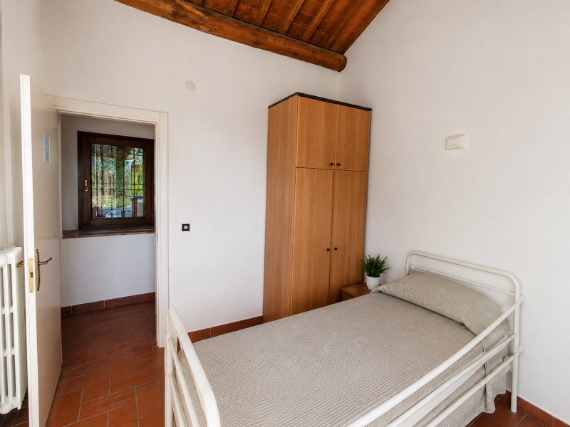Piccola camera da letto con letto singolo, armadio in legno, pareti bianche e pavimento in piastrelle di terracotta.