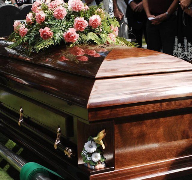 Polished wooden casket with pink and white flowers at a funeral