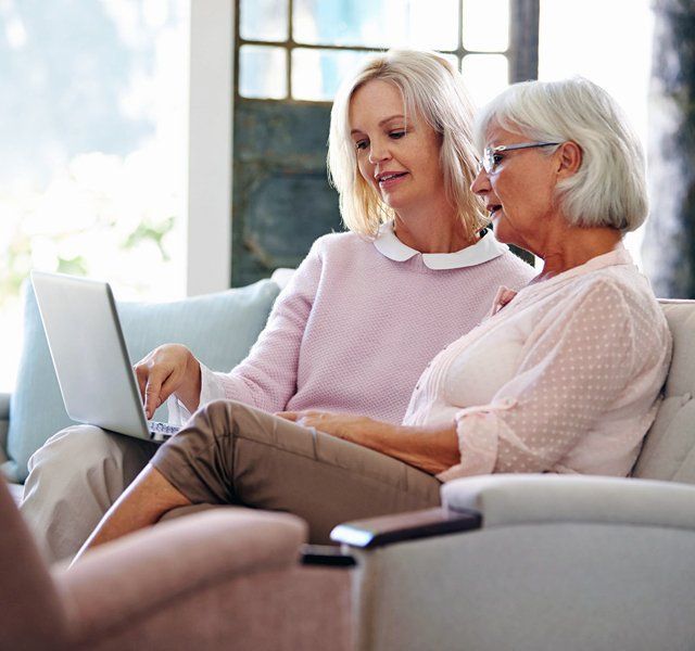 Two women on a couch using a laptop together in a bright living room
