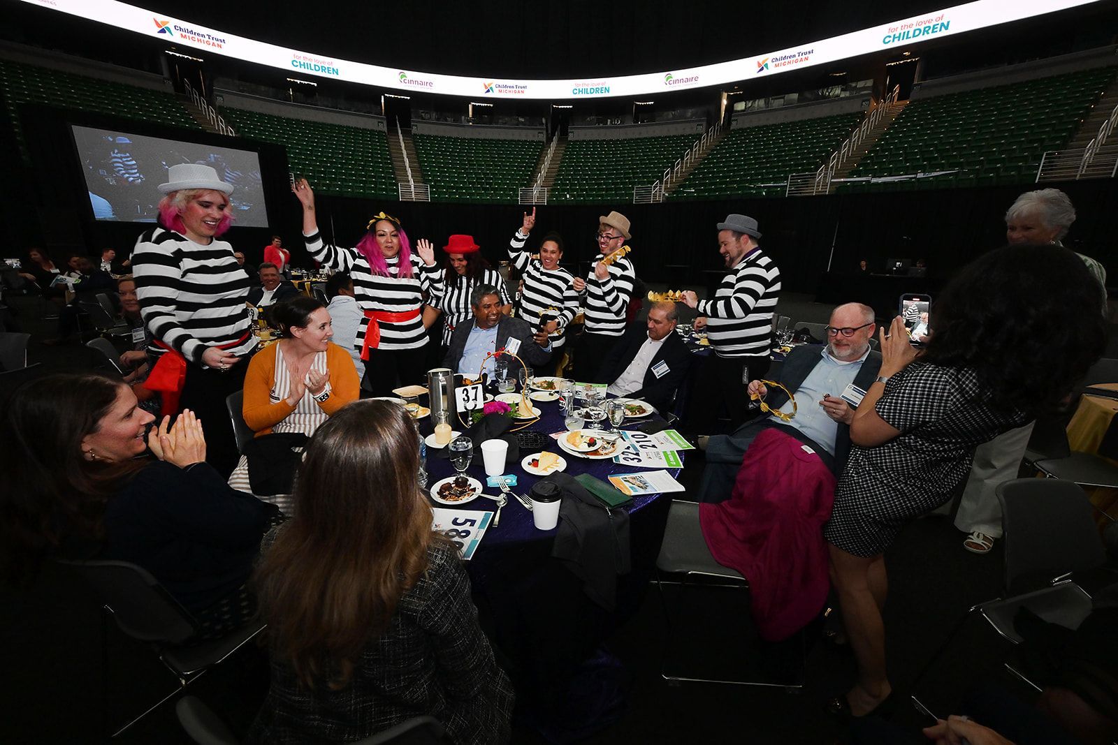 A group in black and white striped shirts celebrates at a table in a dimly lit arena.