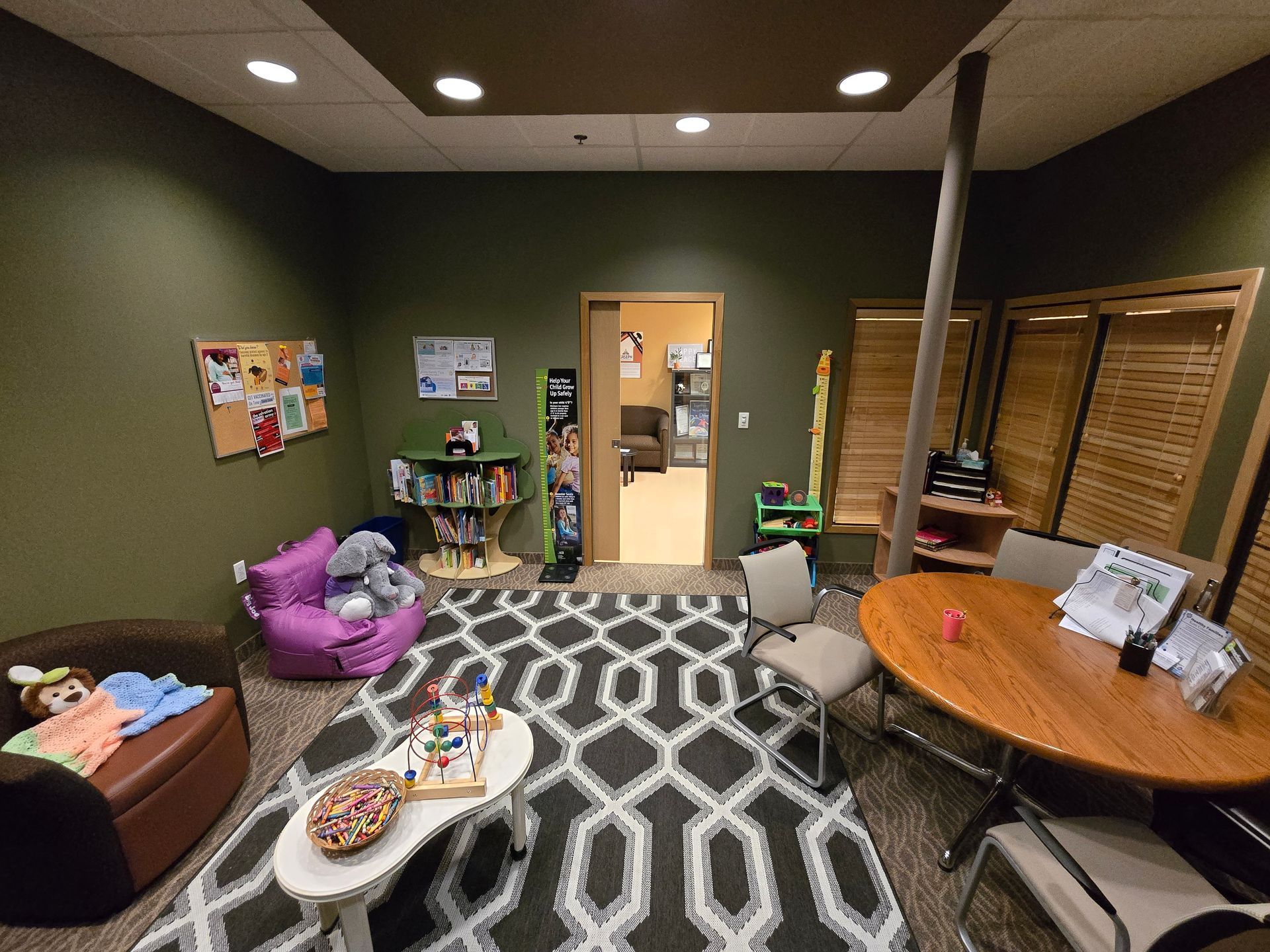 A cozy office playroom with a patterned rug, a purple beanbag chair, a small table with toys, and a circular wooden desk.