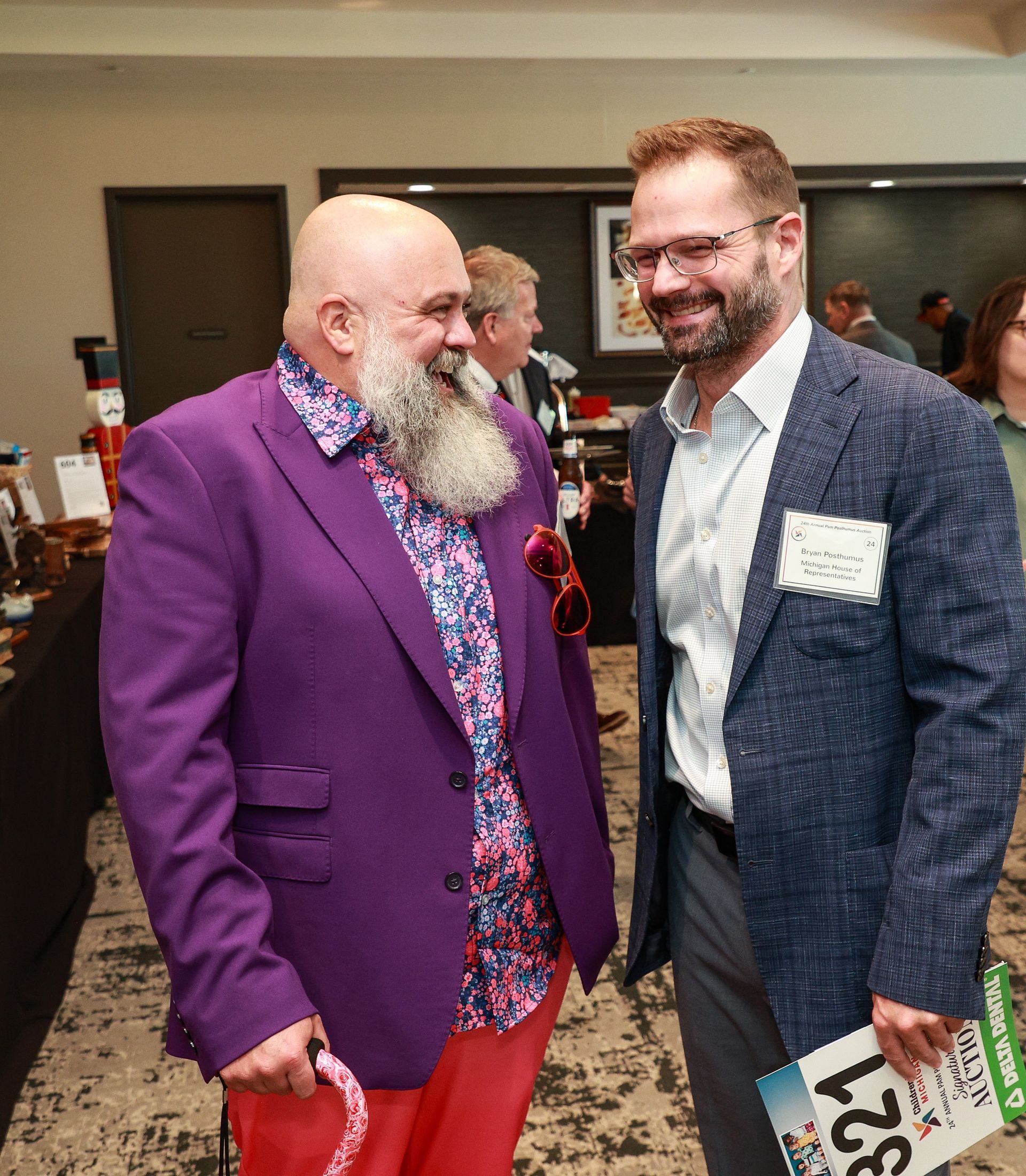 Two men in bright suits smiling at a social event, one in purple and one in blue.