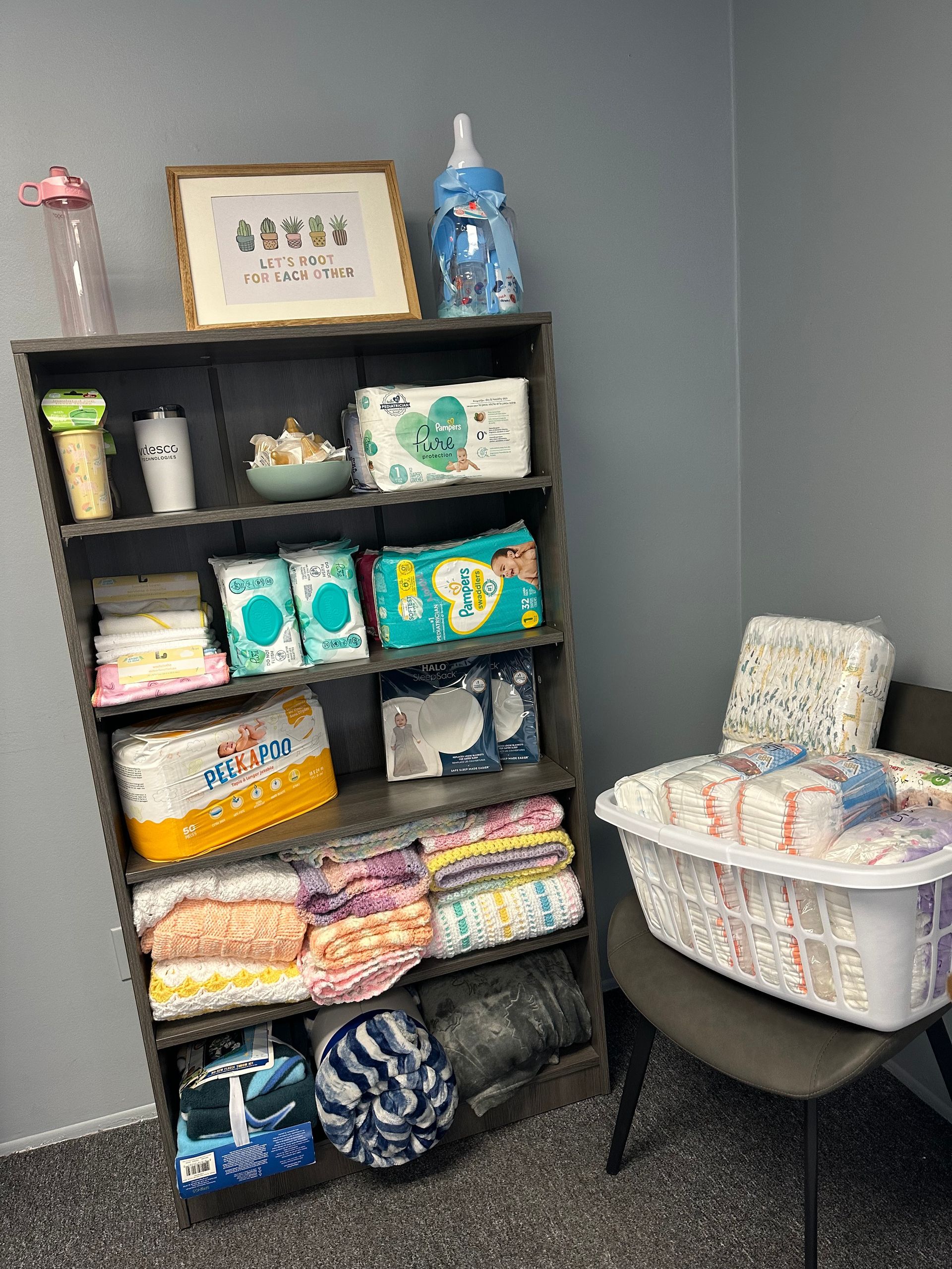 A dark wooden shelving unit filled with baby supplies, including diapers, wipes, and blankets, next to a basket of diapers.