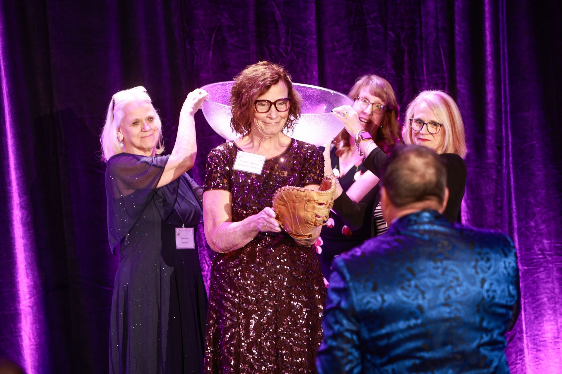 Award ceremony onstage with four people under purple lights; one holds a trophy while another faces them.