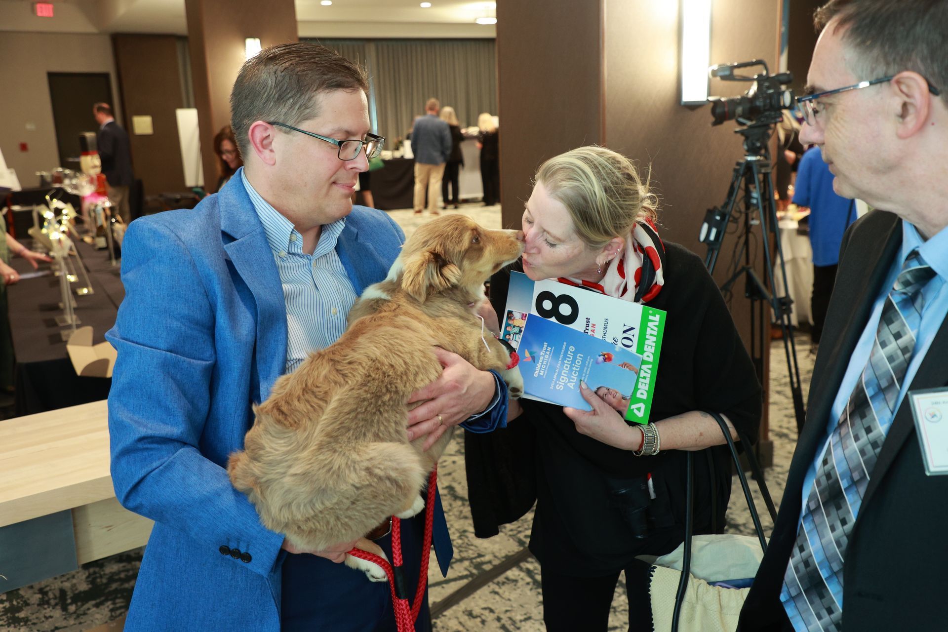 People at a conference pet a fluffy orange cat while one holds a sign.