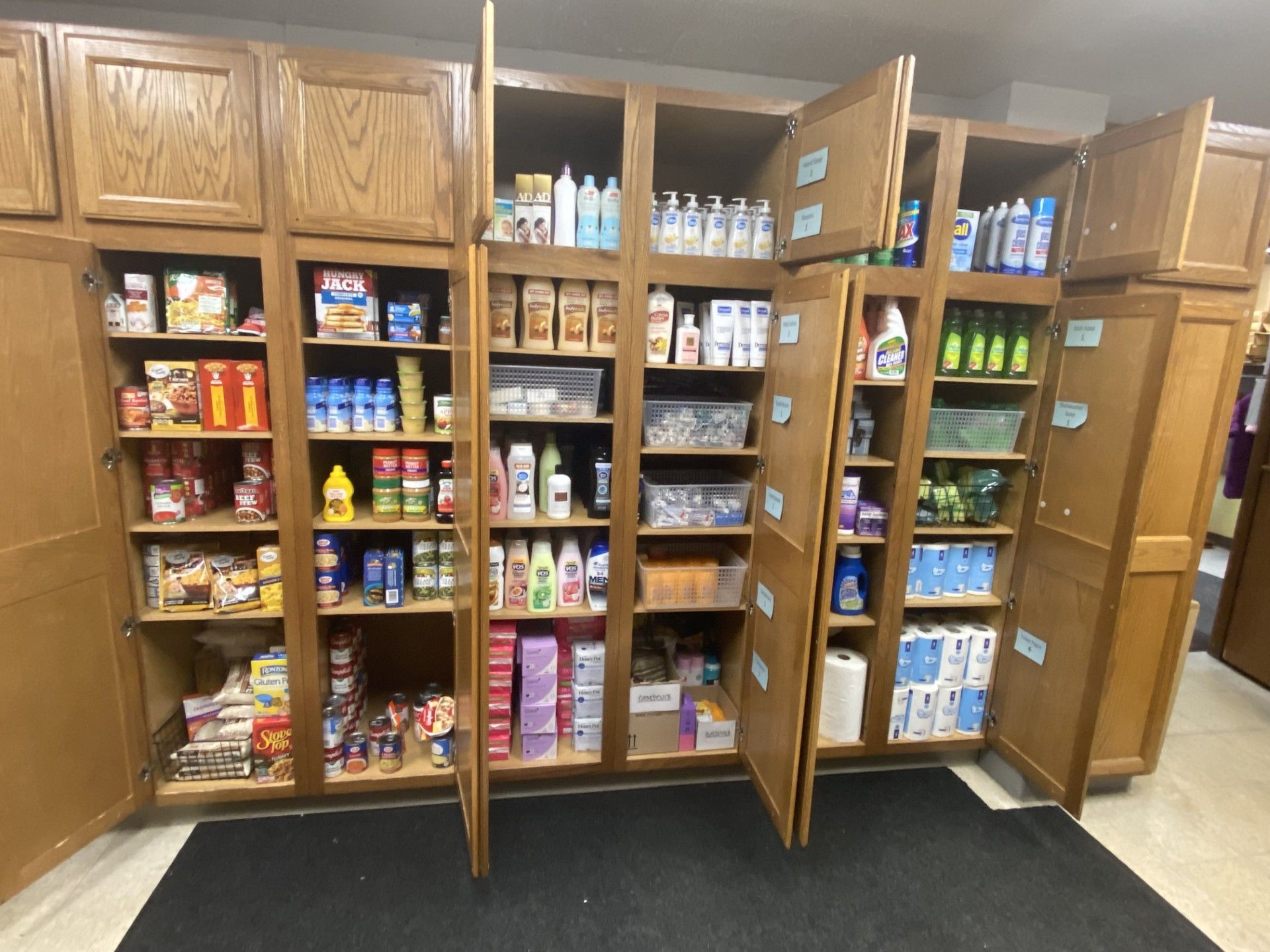 Tall, wood-paneled cabinets organized with various pantry food items, cleaning supplies, and personal care products.