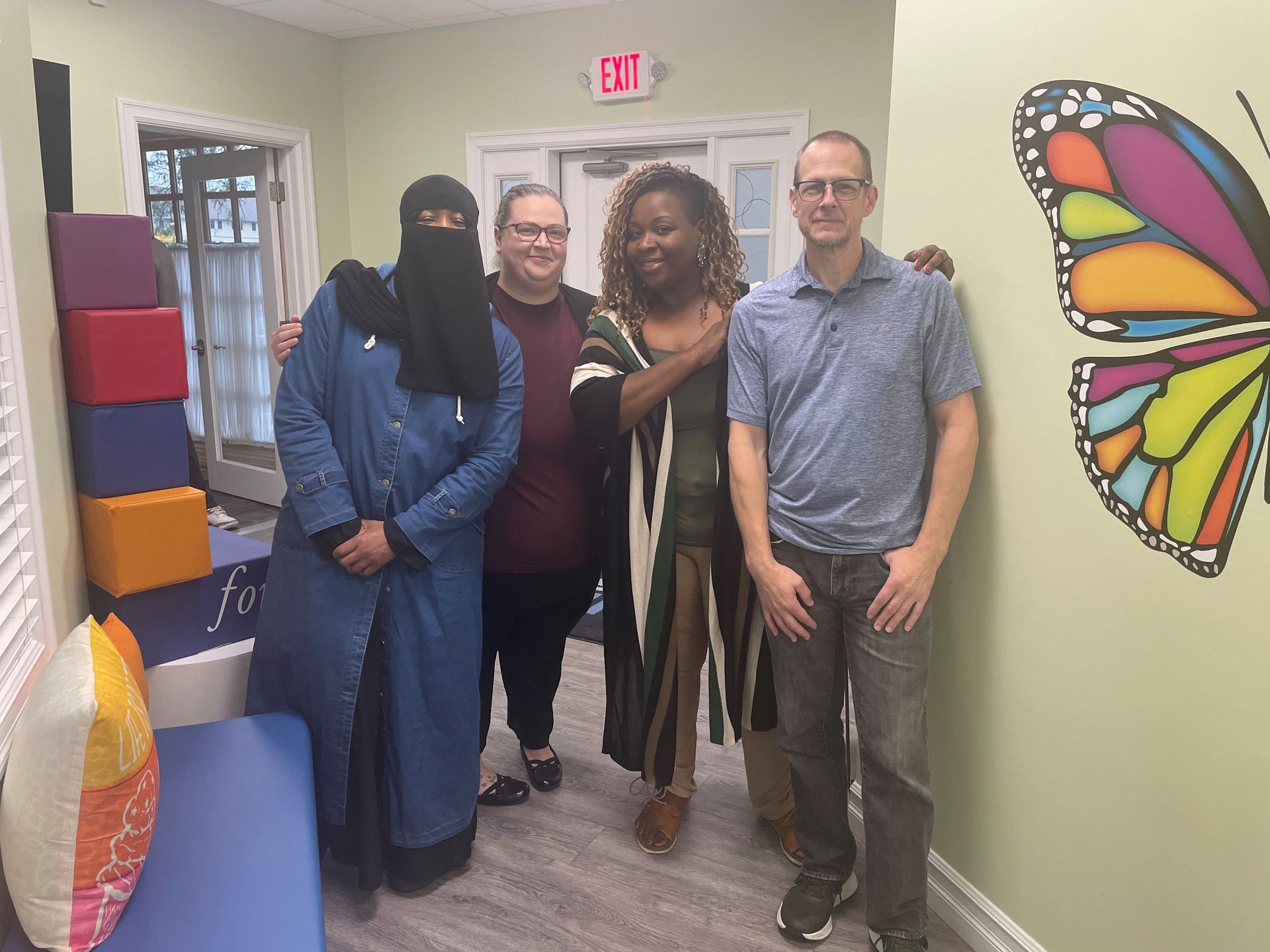 Four people stand smiling together in an office hallway with a colorful butterfly wall mural.
