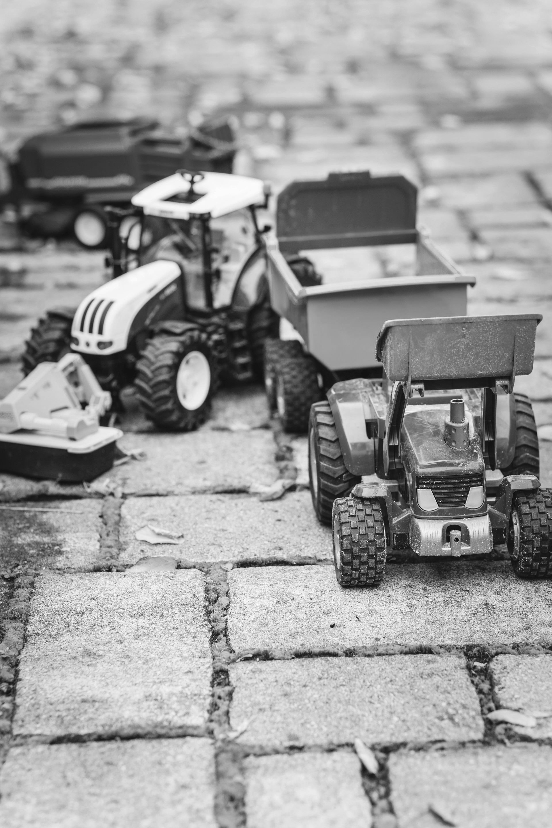 Three toy tractors and a small trailer are arranged on a paved surface.