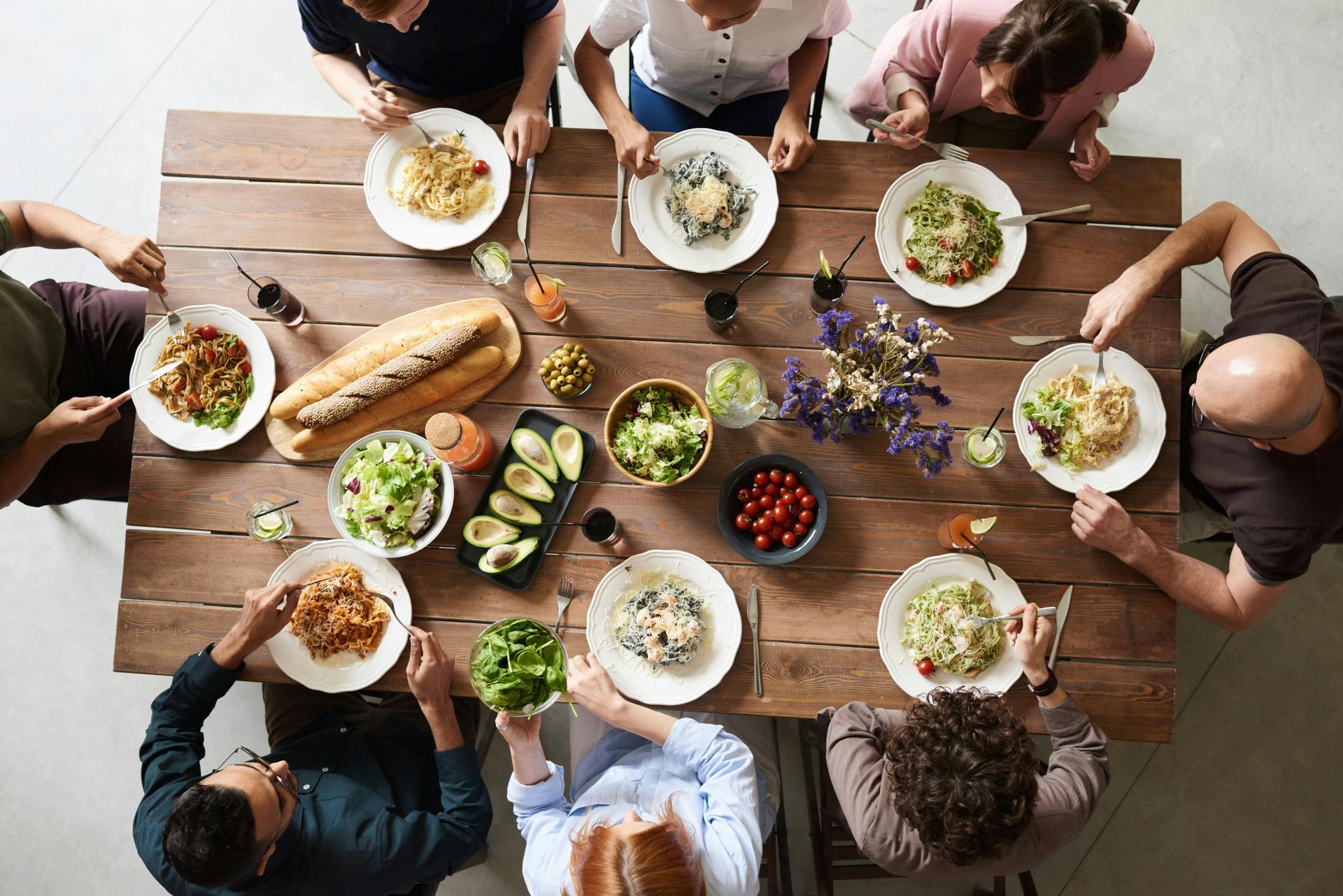 A top-down view of seven people sitting around a rustic wooden table, enjoying a shared meal with various dishes.