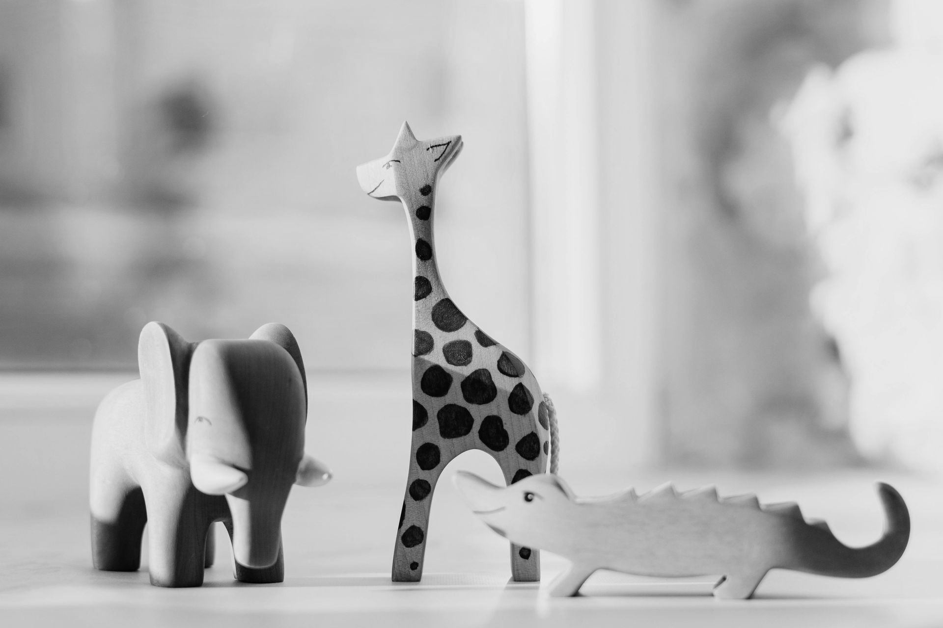 Three wooden animal figures—an elephant, a giraffe, and a crocodile—stand on a light-colored surface.