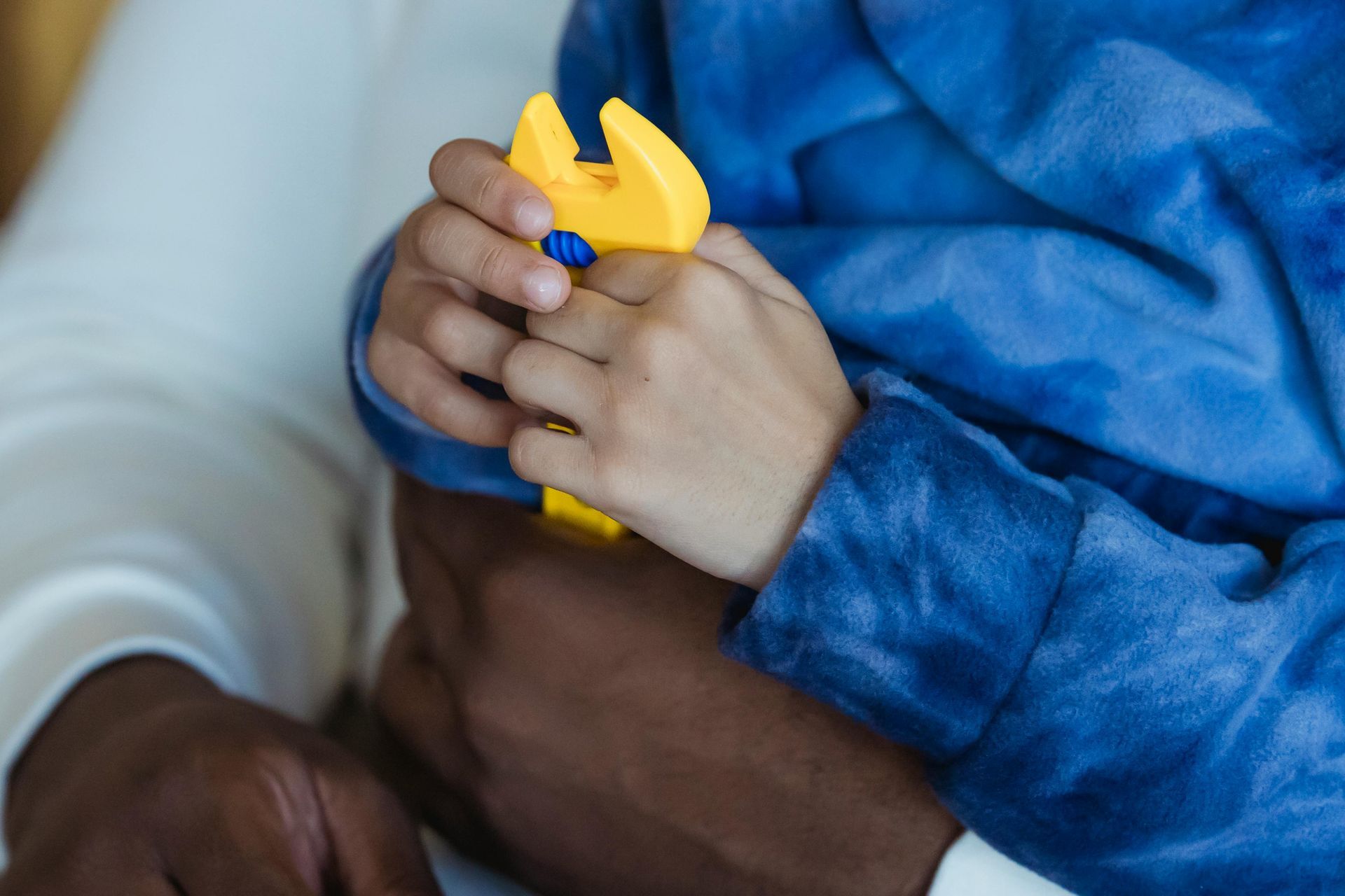 A close-up view of hands holding a small, yellow plastic wrench.