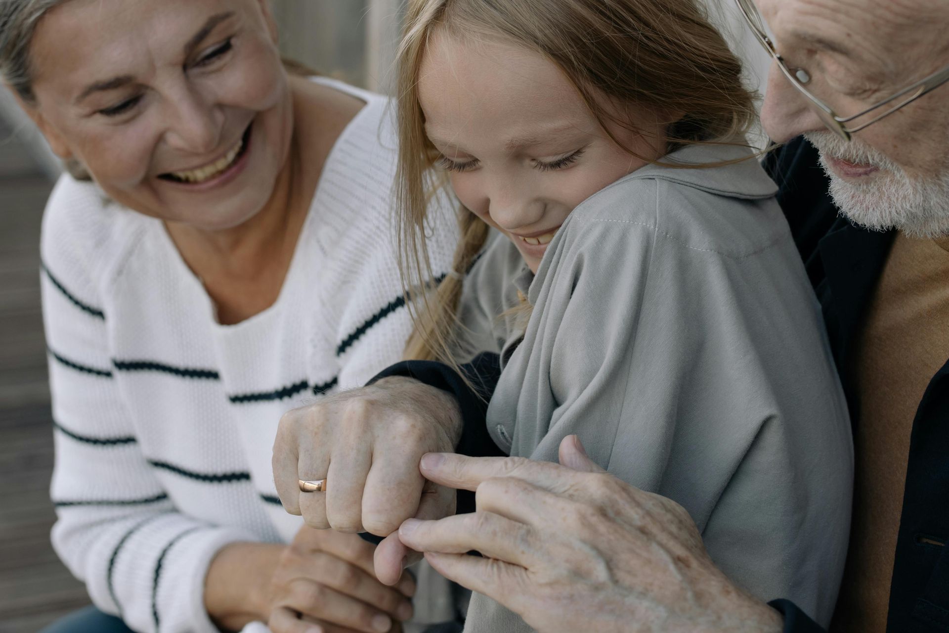 A girl smiling while playing with the hands of two adults.