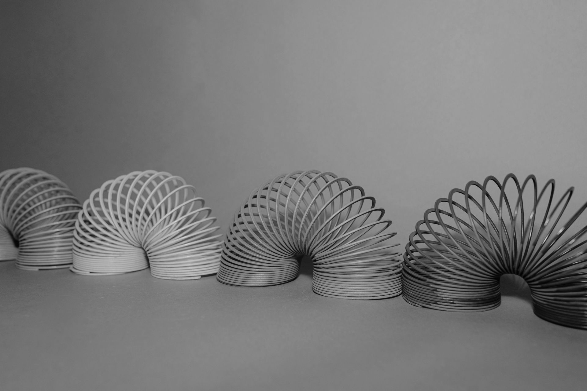 Four Slinky toys are arranged in a horizontal row, transitioning from a light shade on the left to a dark shade on the right.