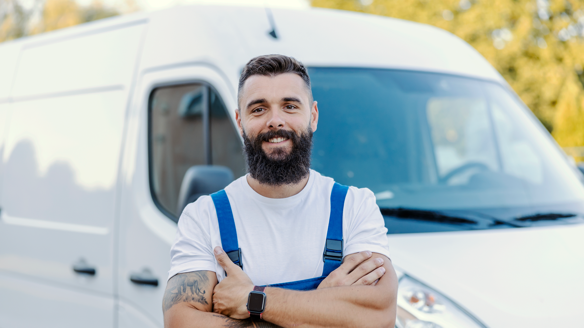 A man with a beard is standing in front of a white van with his arms crossed.