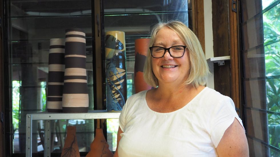 A woman wearing glasses is standing in front of a glass cabinet filled with vases.