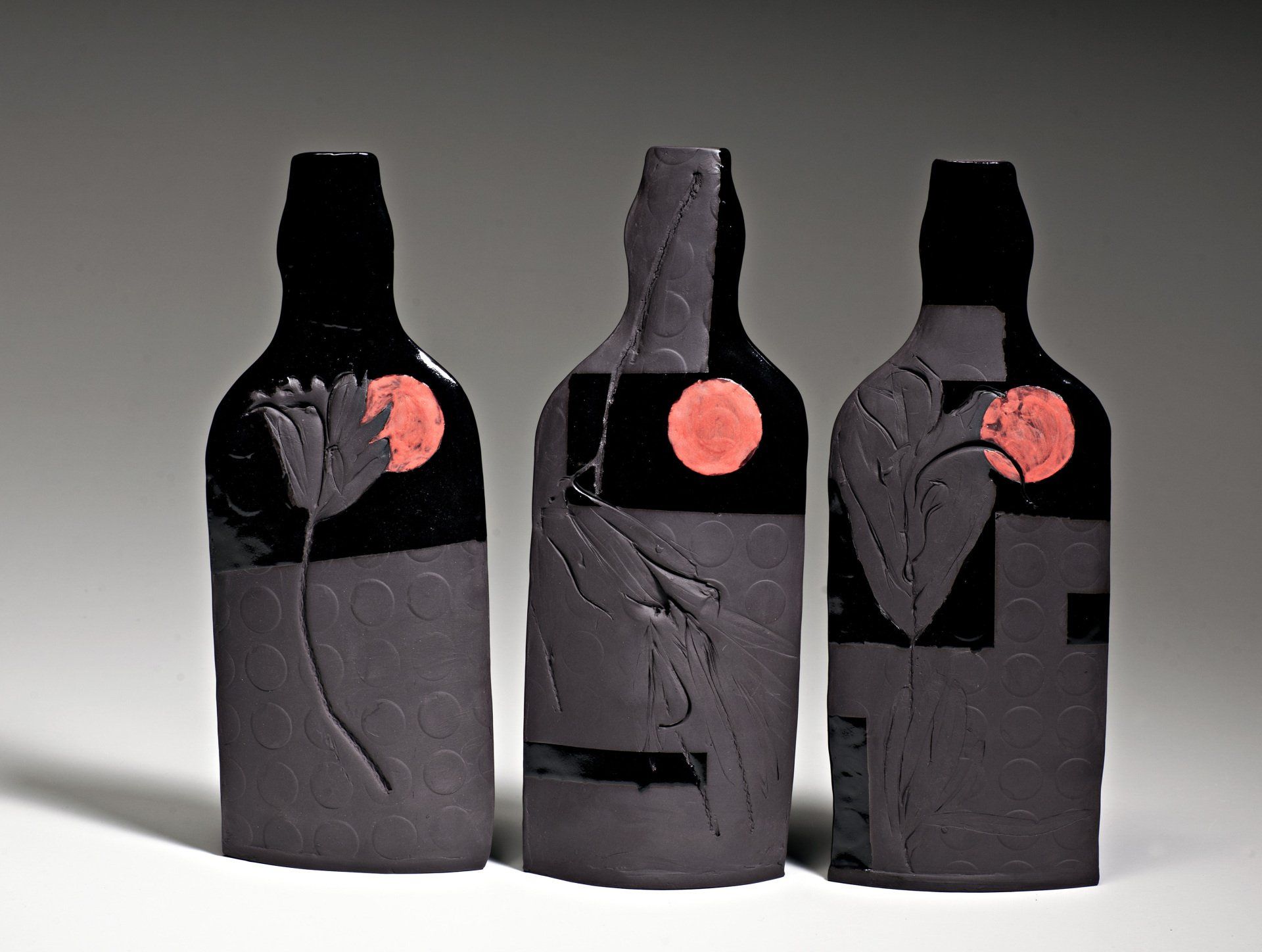 Three black bottles with red flowers on them
