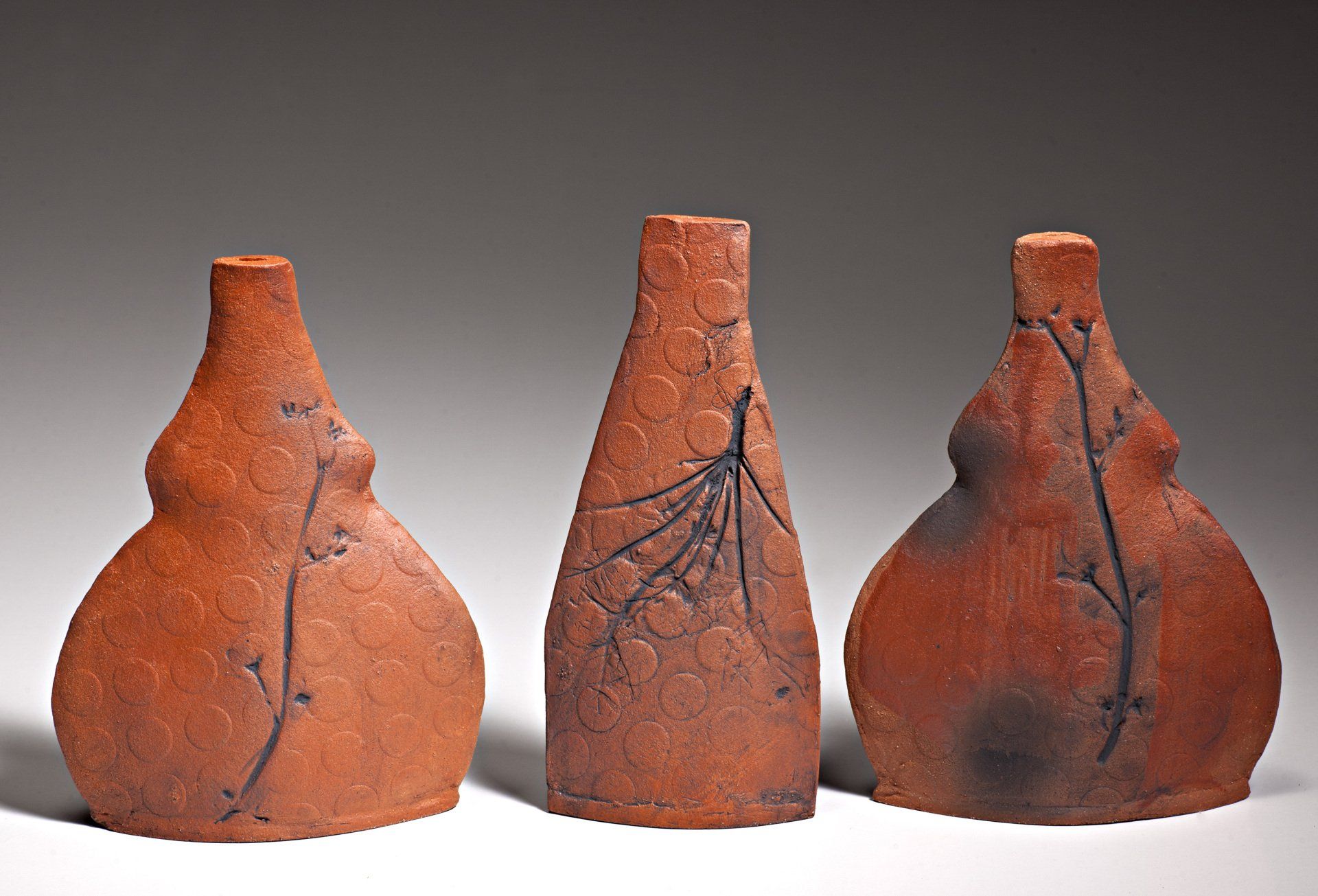 Three clay vases are lined up on a white surface