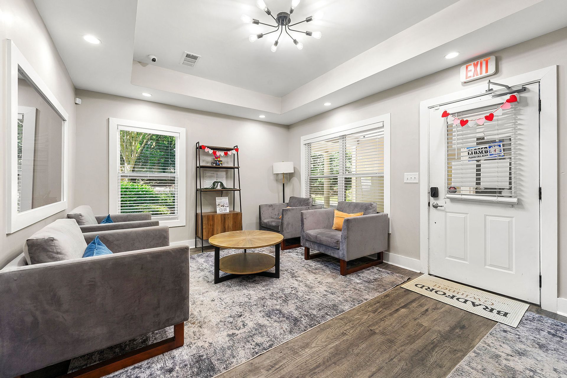 Bright living room with gray couches, coffee table, patterned rug, and front door with fall decor.