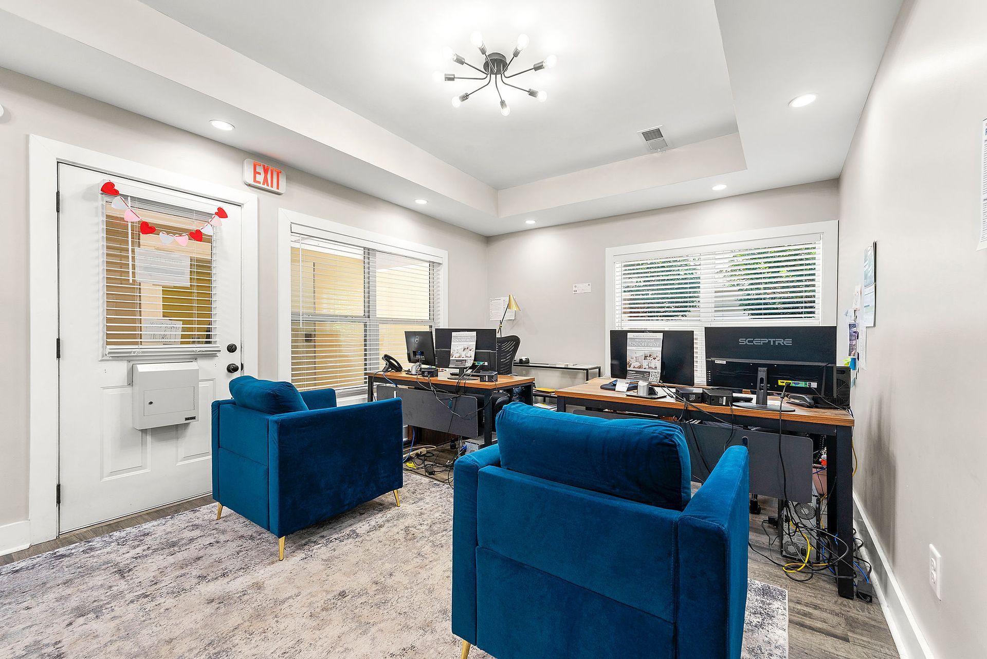 Modern office lounge with blue chairs, desks, computer monitors, and carpeted floor