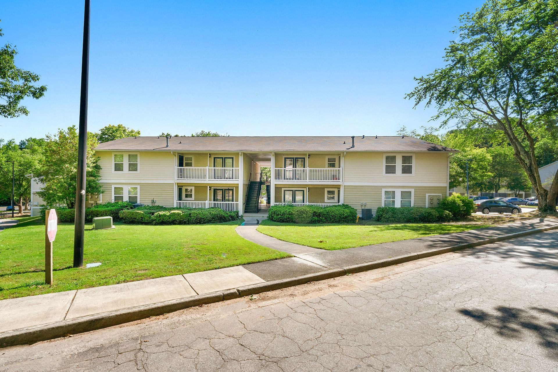 Apartment building with white balconies, green lawn, and a sidewalk on a sunny street