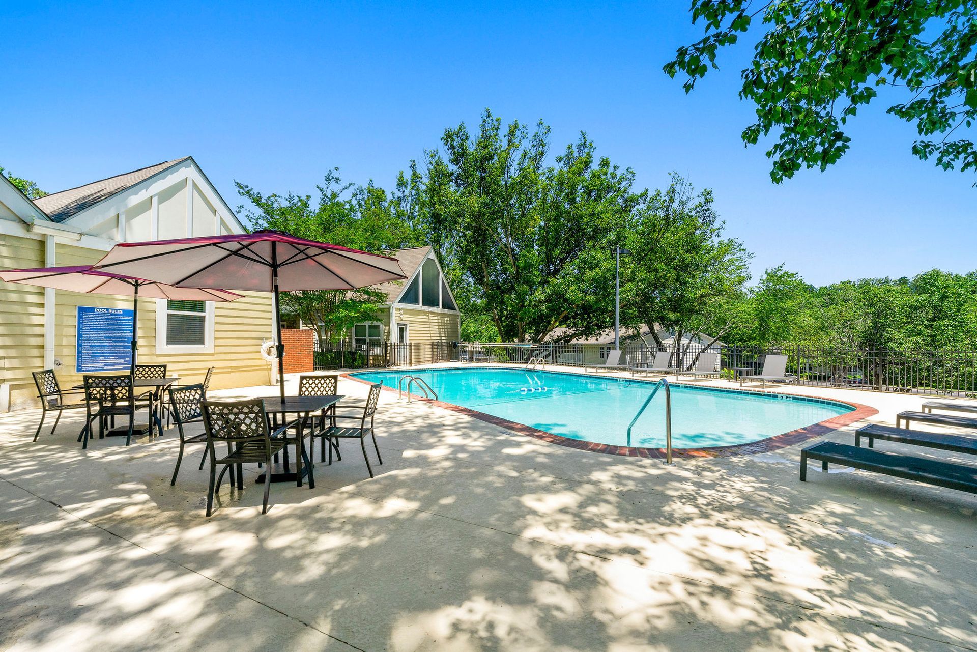 Patio with tables and umbrellas beside a turquoise outdoor pool under a blue sky