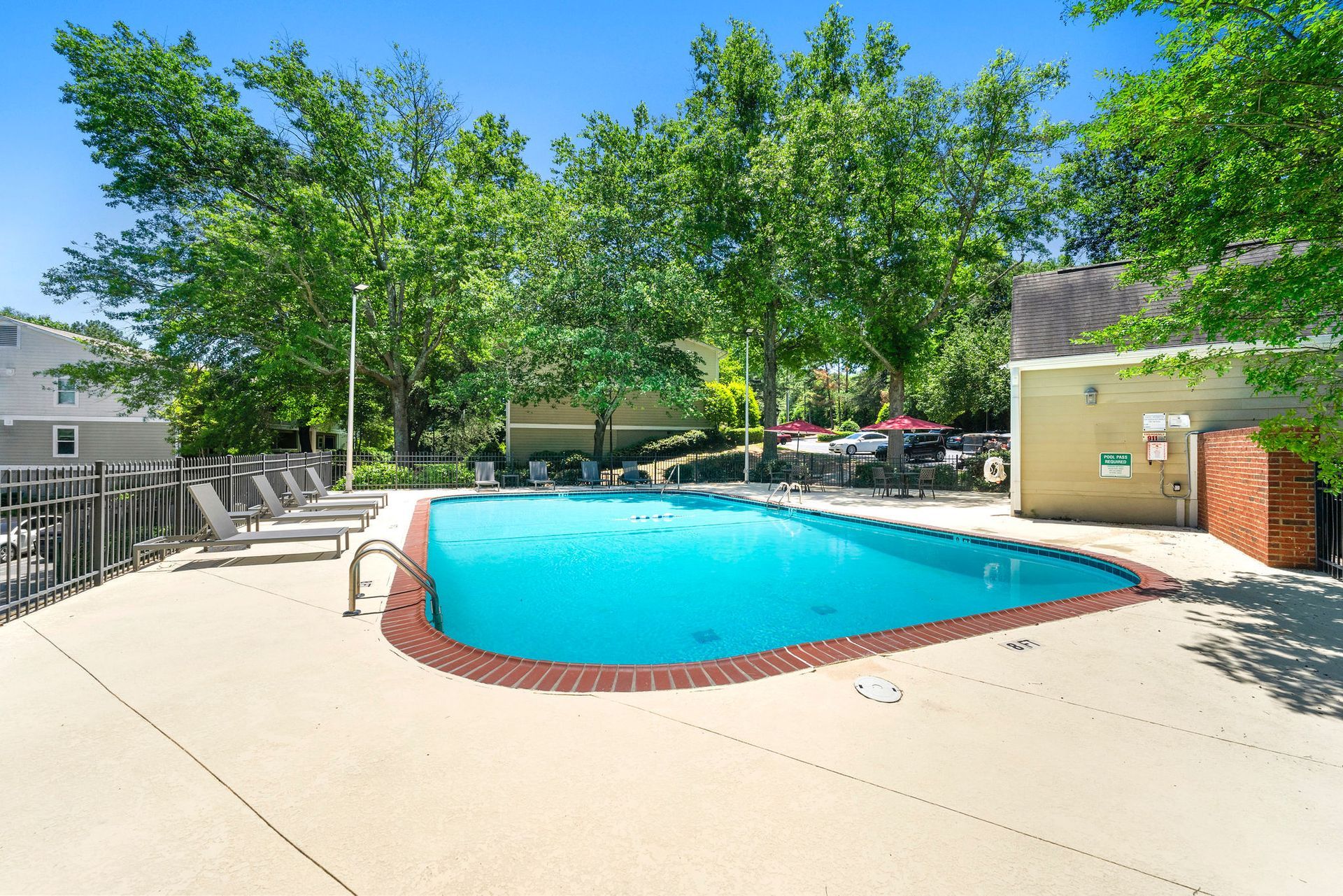 Outdoor apartment pool with turquoise water, surrounded by a concrete deck and trees in bright sunlight