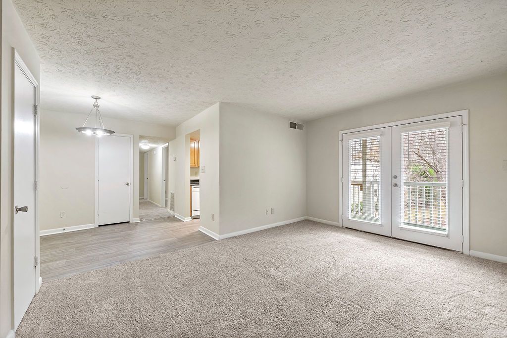 Empty carpeted living room with white walls and sliding glass doors leading to a balcony