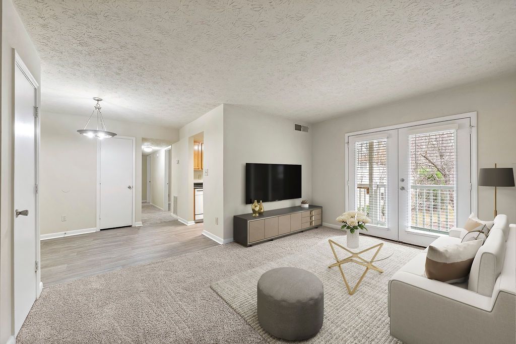 Bright living room with TV, gray sofa, ottoman, and sliding glass doors to a balcony.