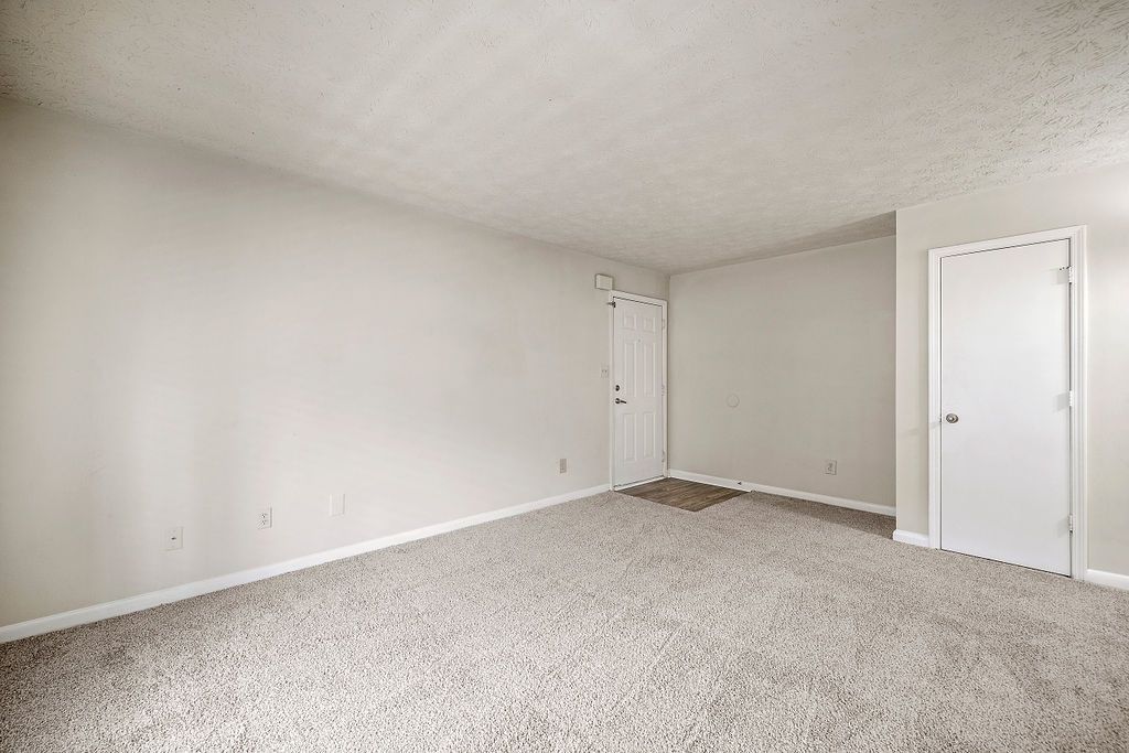 Empty beige carpeted bedroom with white walls and two closed white doors