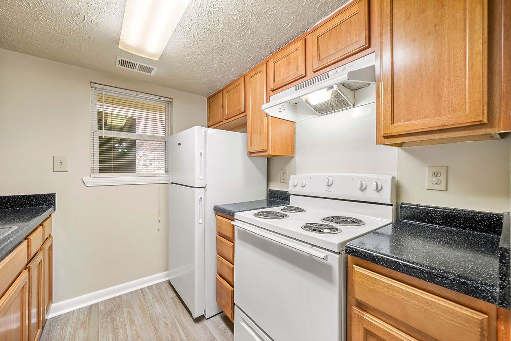 Small kitchen with white appliances, wood cabinets, black countertops, and a window above the sink.