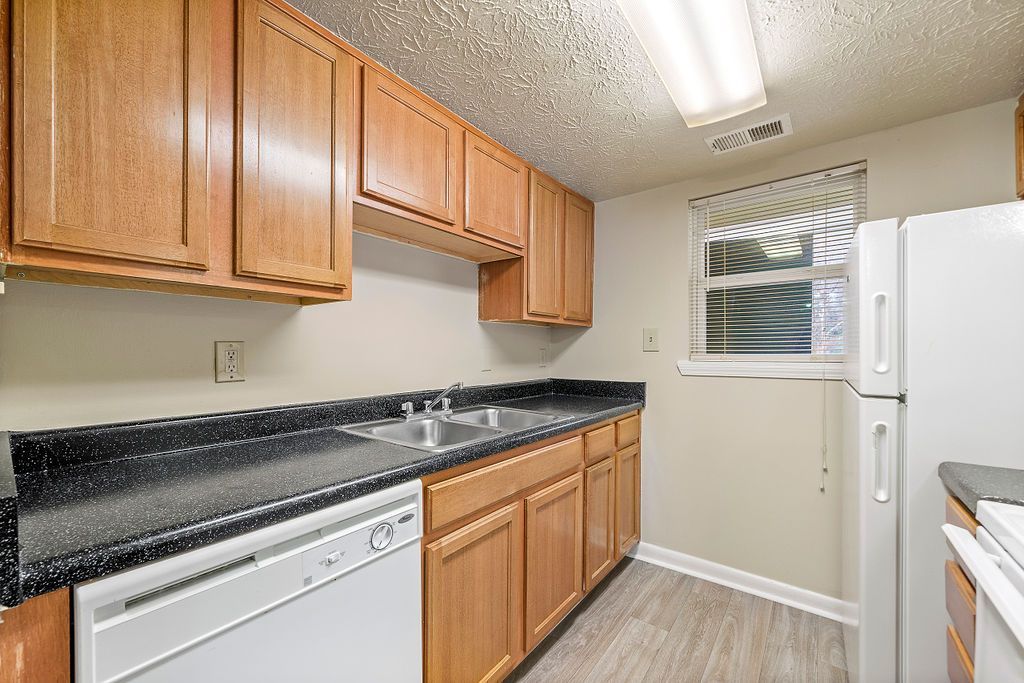 Small kitchen with wood cabinets, black countertops, dishwasher, and window over a sink.
