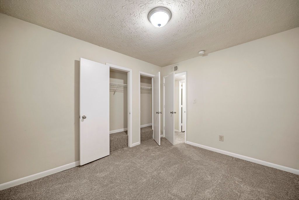 Empty beige bedroom with carpet, closet doors, and a ceiling light