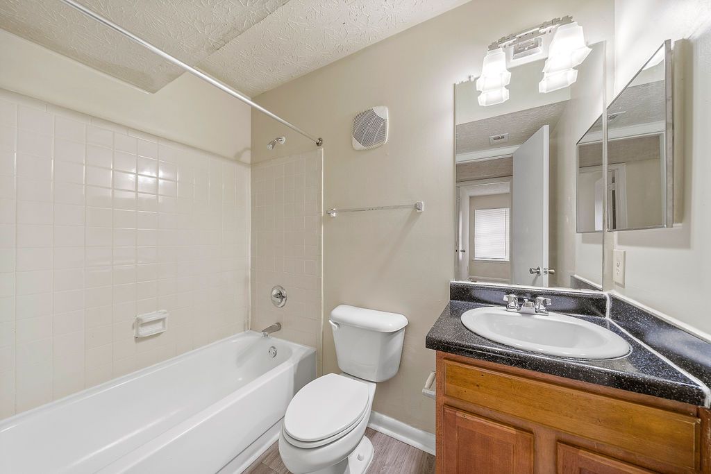 Small beige bathroom with tub, toilet, vanity sink, and mirror.