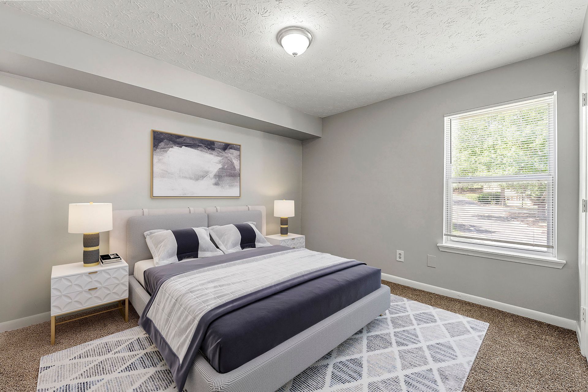 Bright gray bedroom with a neatly made bed, two nightstands, wall art, and a sunlit window.