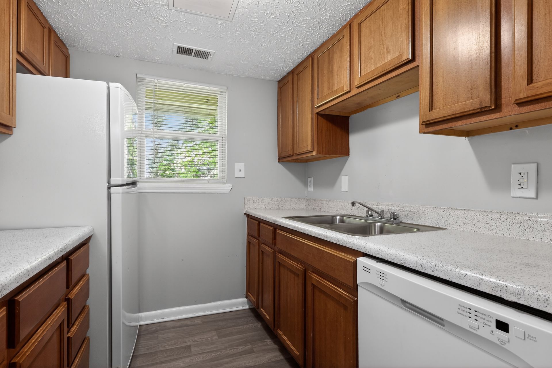 Small galley kitchen with wood cabinets, white appliances, and a window over the sink.