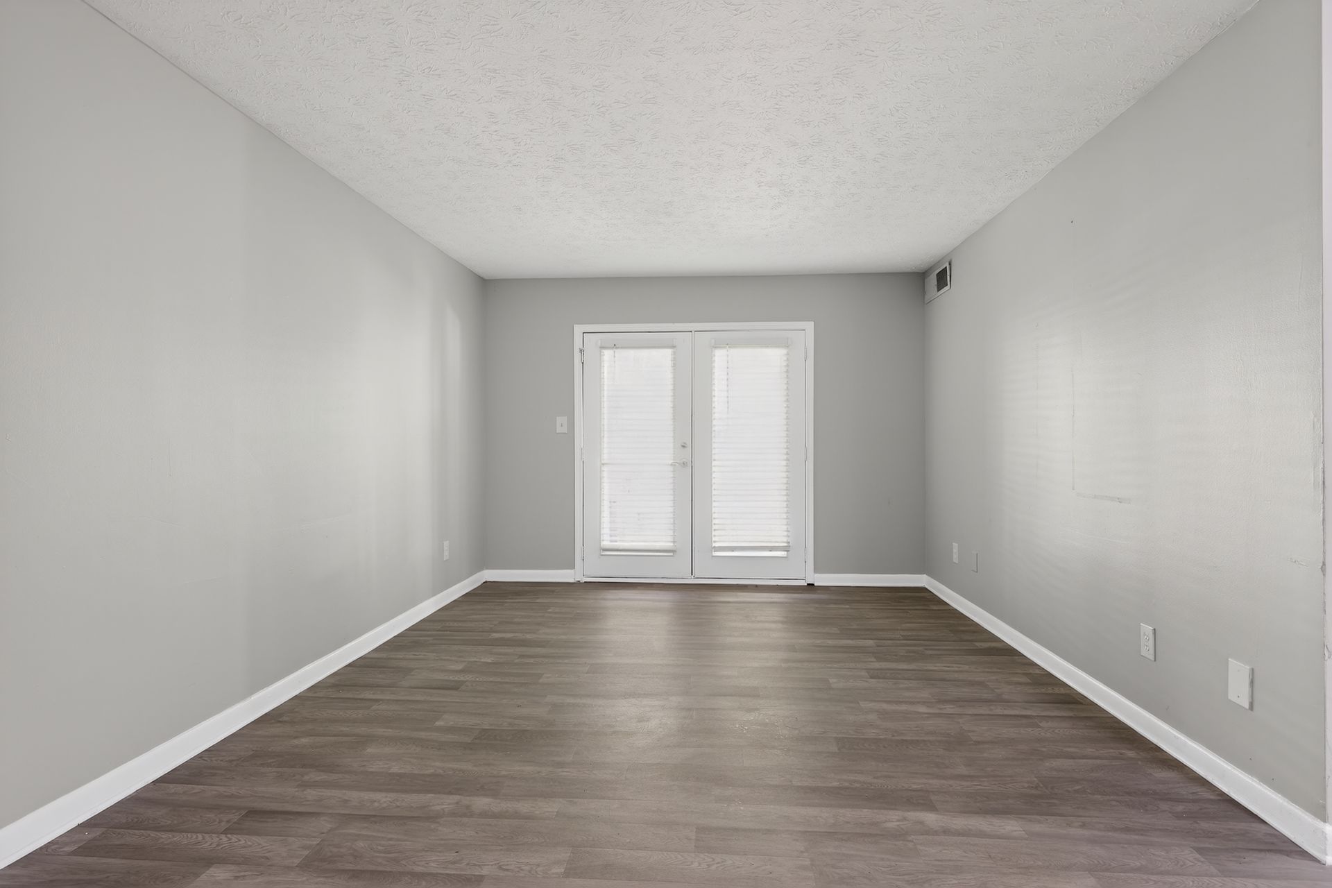 Empty gray room with wood flooring and white French doors at the far end