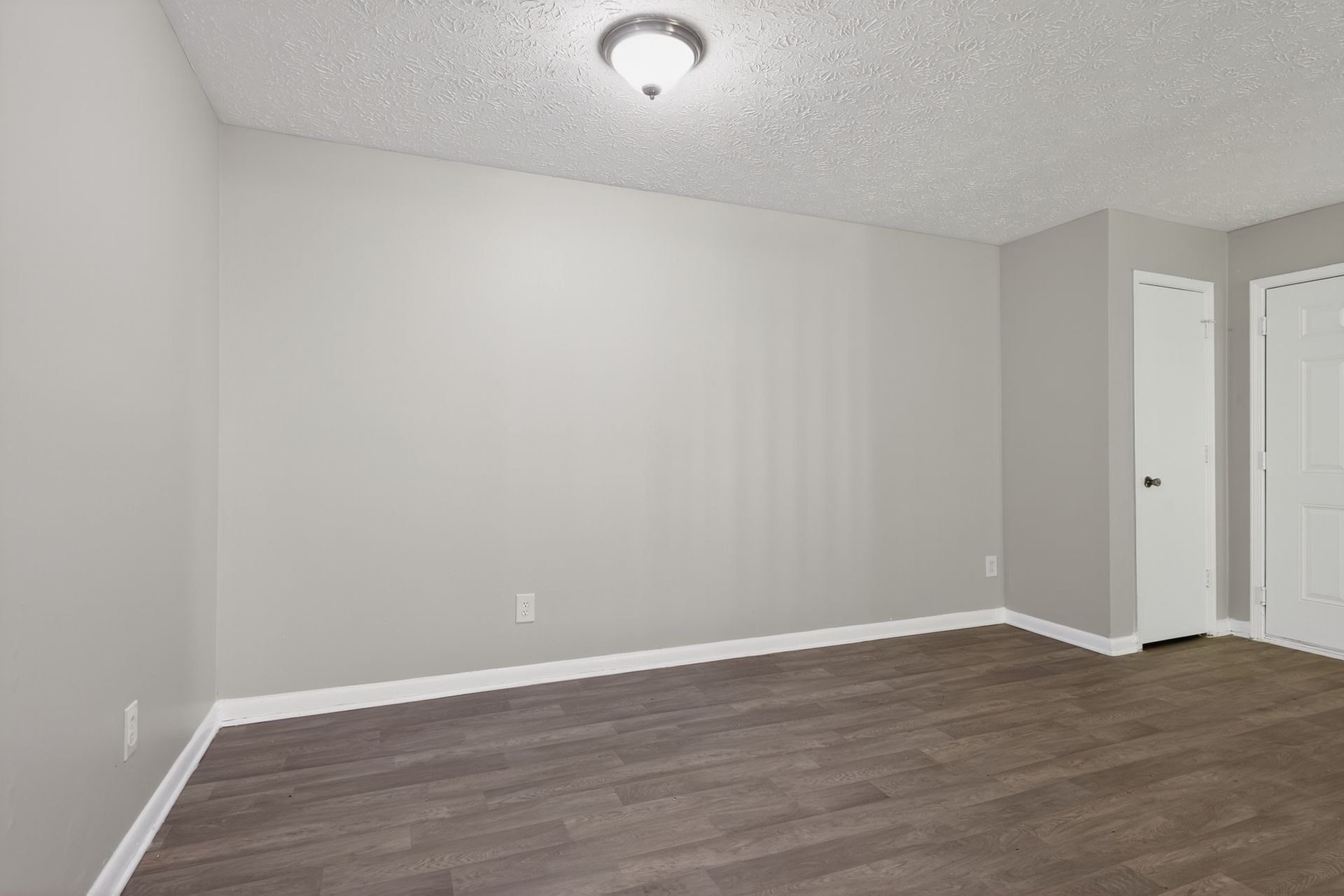Empty gray bedroom with wood flooring, white trim, and a closet door