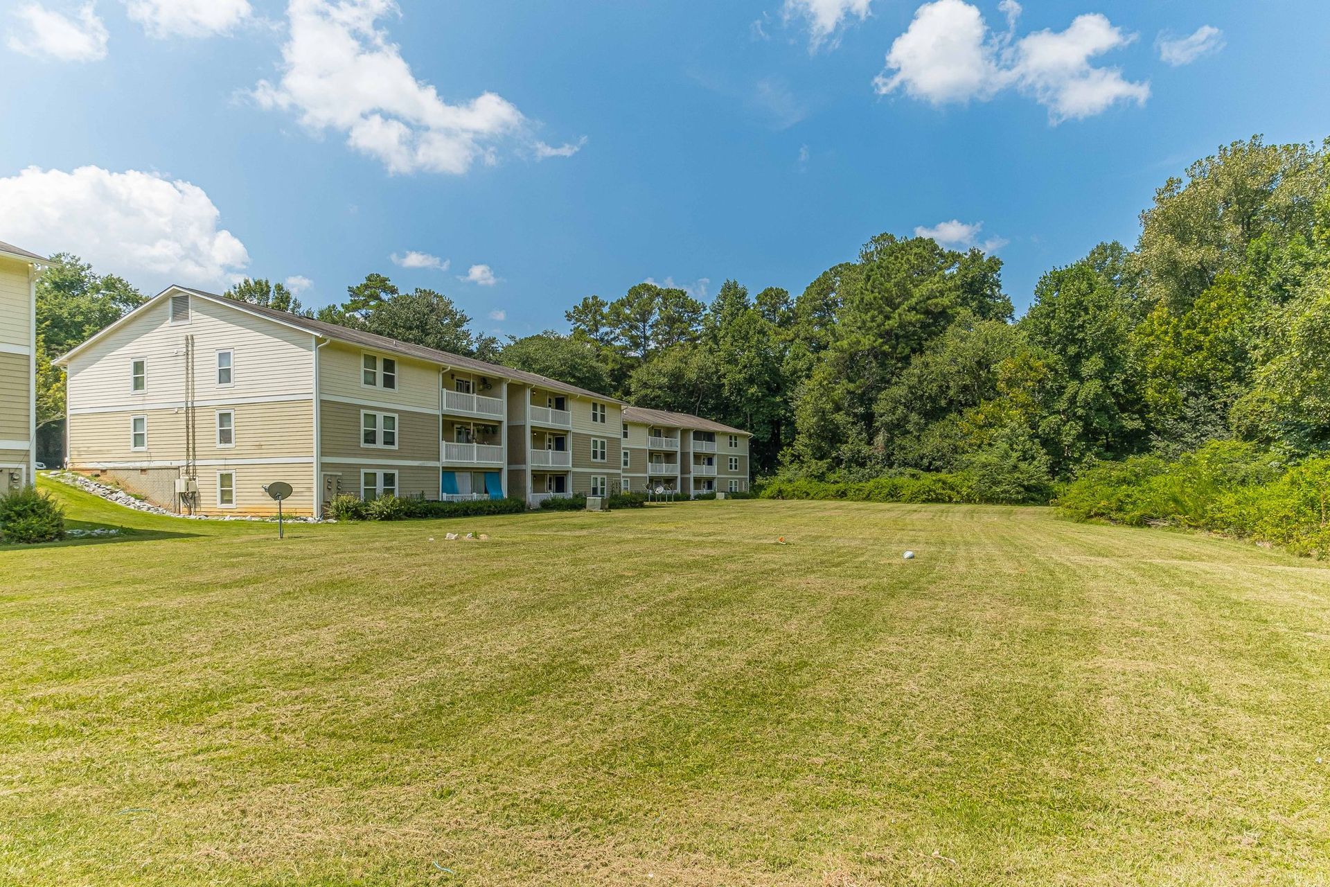 Apartment building beside a grassy lawn and trees under a blue sky