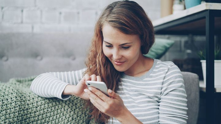 Woman smiling at a smartphone on a couch in a bright living room