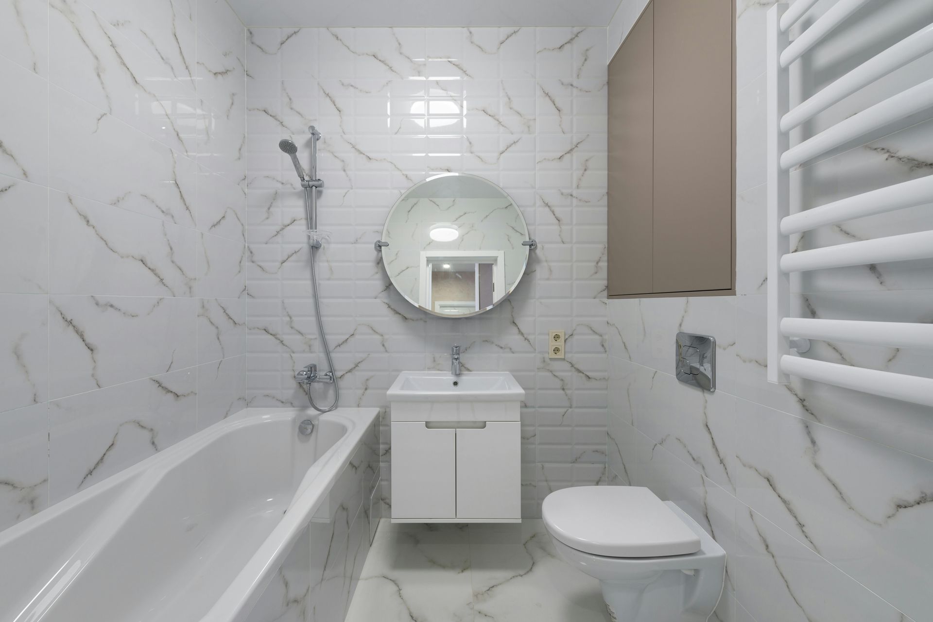 Modern bathroom with white marble-look tiles, bathtub, toilet, vanity, round mirror, and towel rack.